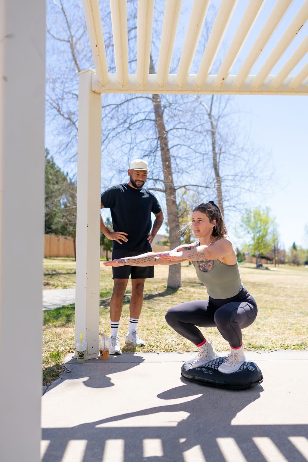 A coach standing back with hands on hips, watching a client hold the bottom of a squat on a BALEROboard