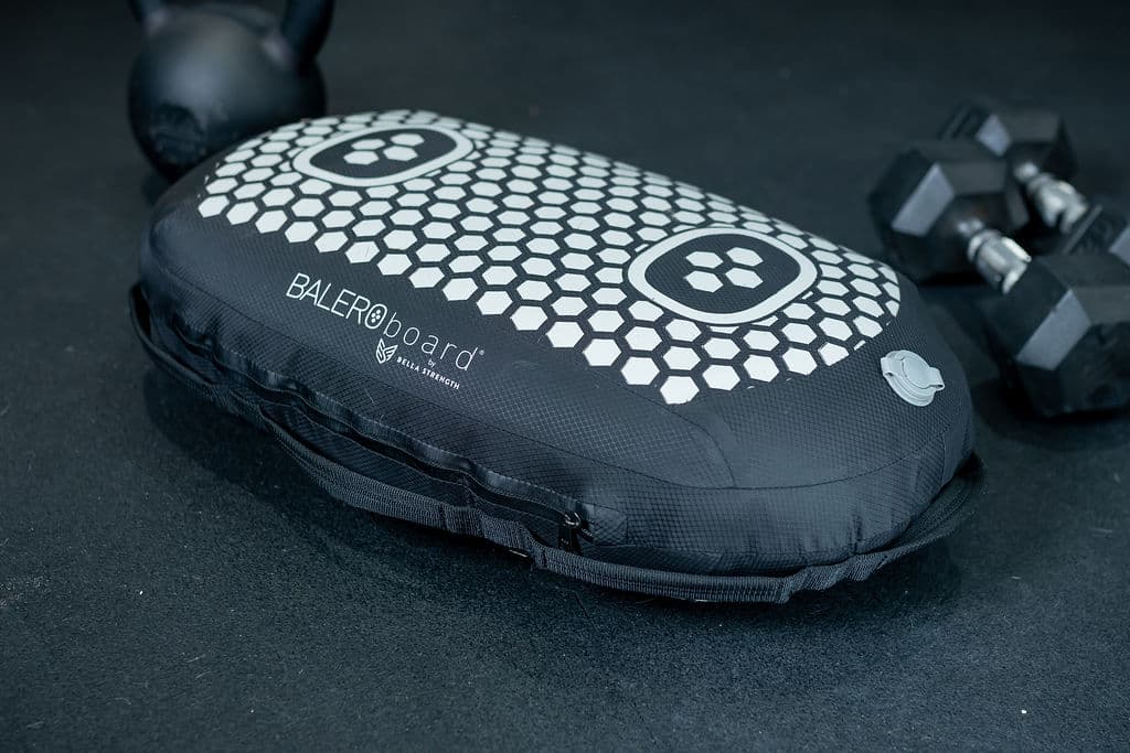 BALEROboard resting on a rubber gym floor beside dumbbells and a kettlebell