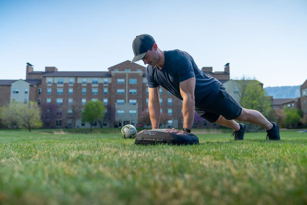 A man in a push-up position with both hands planted on a BALEROboard on grass