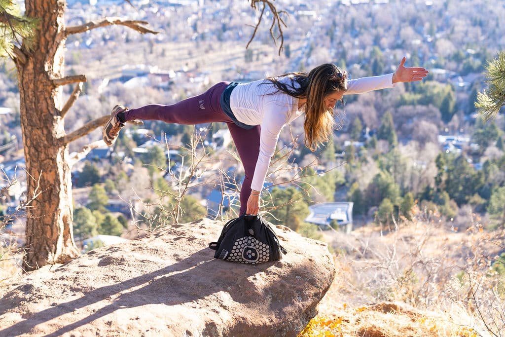 A woman balancing on one leg on a BALEROboard set on a rock ledge above Boulder